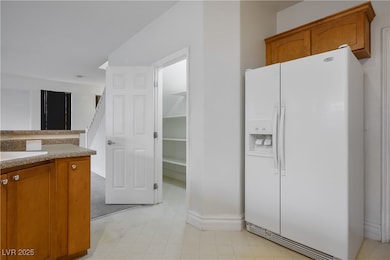 Kitchen with brown cabinetry, white refrigerator with ice dispenser, and light flooring