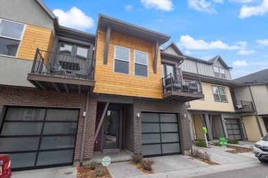 Contemporary house with a balcony, driveway, an attached garage, and brick siding
