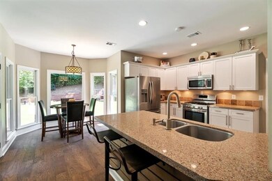Kitchen with appliances with stainless steel finishes, real wood finished floors, white cabinets, light stone counters, and pendant lighting