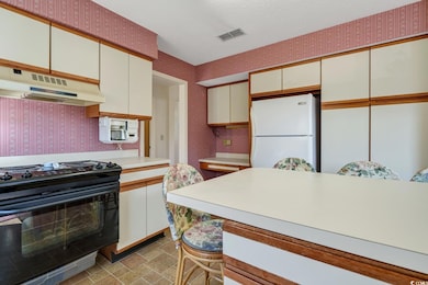 Kitchen with black range oven, freestanding refrigerator, under cabinet range hood, wallpapered walls, and light countertops