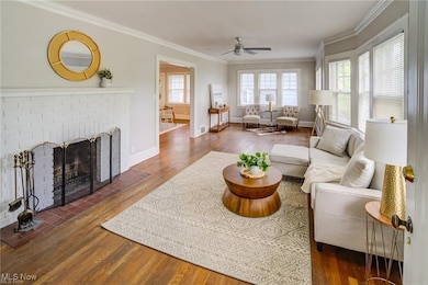 Living area featuring dark wood-type flooring, a brick fireplace, crown molding, and a ceiling fan