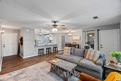 Living room featuring dark wood-type flooring, ceiling fan with notable chandelier, and a textured ceiling