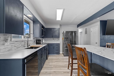 Kitchen featuring stainless steel fridge, range with electric cooktop, black dishwasher, light wood-style flooring, and tasteful backsplash
