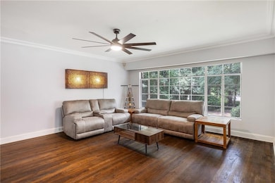 Living area featuring crown molding, dark wood-type flooring, and a ceiling fan