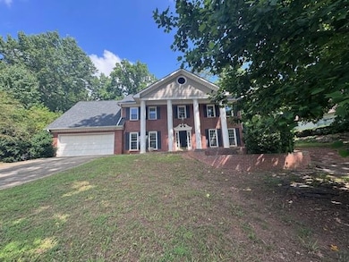 Greek revival house featuring a garage, concrete driveway, a front lawn, and brick siding