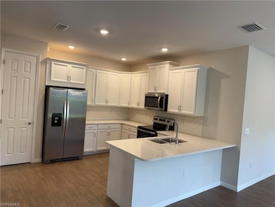 Kitchen with appliances with stainless steel finishes, a sink, dark wood-style flooring, light countertops, and white cabinetry