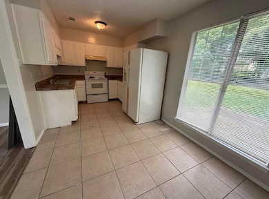Kitchen featuring dark countertops, white appliances, a textured ceiling, white cabinetry, and light tile patterned flooring