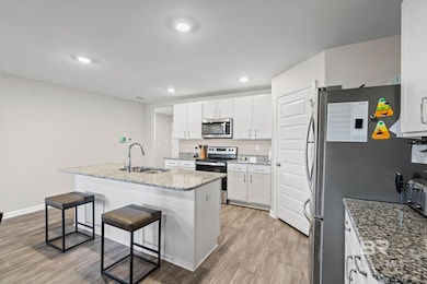 Kitchen featuring light wood-type flooring, light stone countertops, appliances with stainless steel finishes, a center island with sink, and recessed lighting