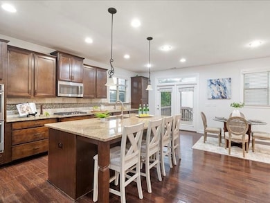 Kitchen with stainless steel microwave, light stone counters, a kitchen island with sink, dark wood-type flooring, and a kitchen bar