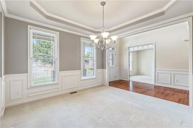 Formal dining area raised ceiling, a chandelier, a wainscoted wall, and crown molding