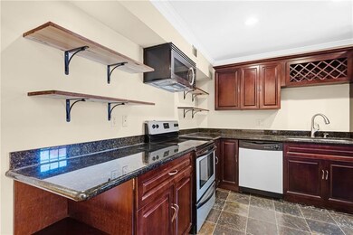 Kitchen with open shelves, reddish brown cabinets, stainless steel appliances, dark stone counters, and crown molding