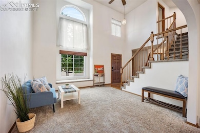Carpeted entrance foyer featuring plenty of natural light, stairway, a towering ceiling, arched walkways, and a ceiling fan