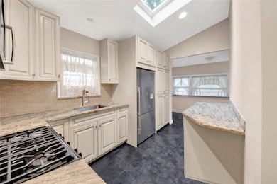 Kitchen with a sink, stainless steel fridge with ice dispenser, decorative backsplash, a skylight, and light stone countertops