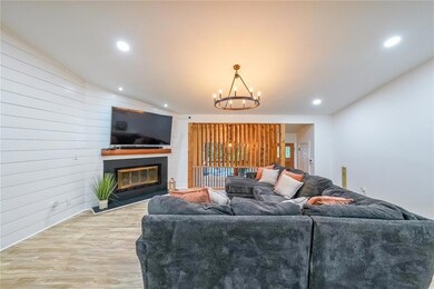 Living room featuring light wood-style flooring, a glass covered fireplace, a chandelier, wood walls, and vaulted ceiling