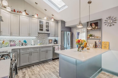 Kitchen featuring lofted ceiling, hanging light fixtures, gray cabinets, backsplash, and stainless steel appliances