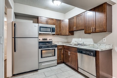 Kitchen featuring stainless steel appliances, light countertops, dark brown cabinetry, and light tile patterned floors