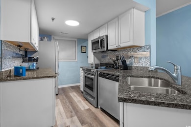 Kitchen featuring white cabinets, backsplash, appliances with stainless steel finishes, light wood finished floors, and dark stone countertops