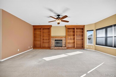 Unfurnished living room featuring a brick fireplace, light colored carpet, ceiling fan, and built in shelves