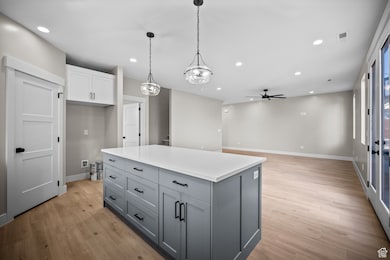 Kitchen with hanging light fixtures, gray cabinetry, a kitchen island, white cabinets, and light wood finished floors
