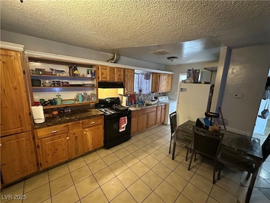 Kitchen featuring black gas range oven, open shelves, light tile patterned flooring, dark countertops, and a textured ceiling