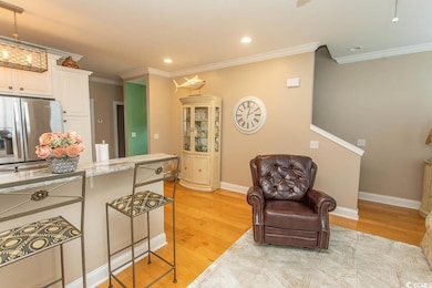 Kitchen featuring stainless steel fridge, light wood-style floors, crown molding, white cabinets, and a kitchen bar