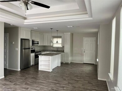 Kitchen featuring a raised ceiling, stainless steel appliances, open shelves, white cabinets, and a ceiling fan