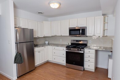 Kitchen with appliances with stainless steel finishes, tasteful backsplash, light wood-type flooring, white cabinets, and light stone counters