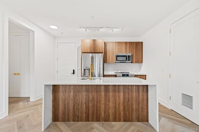 Kitchen with brown cabinetry, light stone counters, modern cabinets, appliances with stainless steel finishes, and an island with sink