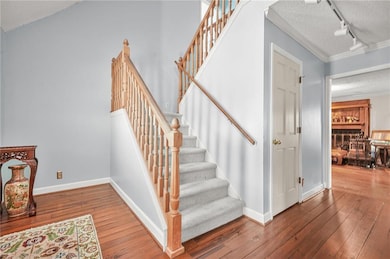 Stairway with track lighting, a textured ceiling, hardwood / wood-style flooring, and ornamental molding