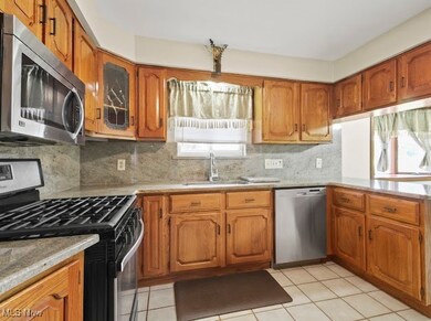 Kitchen featuring stainless steel appliances, decorative backsplash, brown cabinets, and light stone countertops