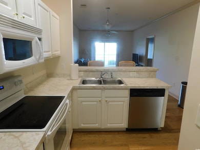 Kitchen featuring white appliances, white cabinets, light countertops, and ornamental molding