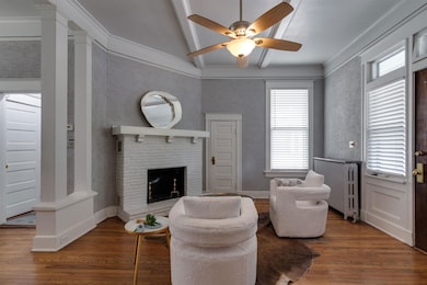 Living room with radiator heating unit, a ceiling fan, wood finished floors, a fireplace, and crown molding