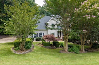 View of property hidden behind natural elements with stucco siding, a shingled roof, and a front yard