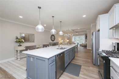 Kitchen featuring coffered ceiling, light wood-type flooring, appliances with stainless steel finishes, decorative light fixtures, and recessed lighting