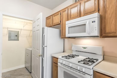 Kitchen featuring white appliances, light countertops, electric panel, brown cabinets, and light wood-style floors