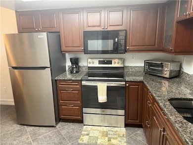 Kitchen featuring stainless steel appliances, glass insert cabinets, dark stone counters, and light tile patterned floors