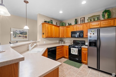 Kitchen featuring black appliances, pendant lighting, a peninsula, brown cabinetry, and light tile patterned floors