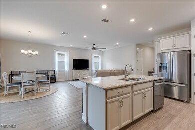Kitchen with light wood-style floors, stainless steel appliances, a kitchen island with sink, open floor plan, and light stone countertops