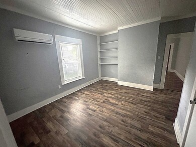 Spare room with a wall mounted air conditioner, dark wood-type flooring, built in features, and baseboards