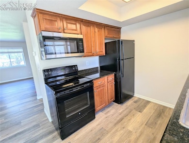 Kitchen featuring black appliances, light wood-type LVP flooring, brown cabinetry, and dark solid surface countertops