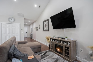 Living room featuring wood finished floors, baseboards, vaulted ceiling, recessed lighting, and a glass covered fireplace