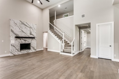 Unfurnished living room featuring a high ceiling, a premium fireplace, light wood-style floors, ceiling fan, and stairway