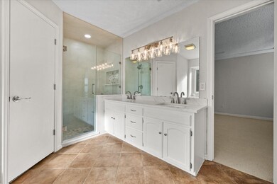 Full bathroom with double vanity, a stall shower, light tile patterned floors, light colored carpet, and a textured ceiling
