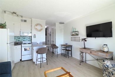 Kitchen featuring white appliances, a kitchen breakfast bar, white cabinets, decorative backsplash, and light wood-style flooring