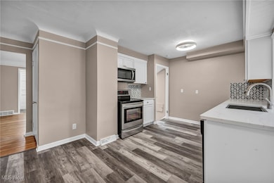 Kitchen featuring appliances with stainless steel finishes, white cabinetry, decorative backsplash, wood finished floors, and light stone counters