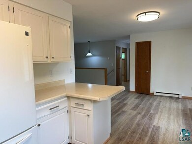 Kitchen with freestanding refrigerator, a baseboard radiator, a peninsula, white cabinets, and wood finished floors