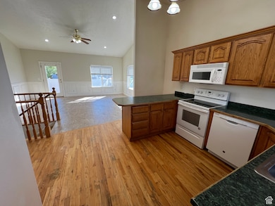 Kitchen with brown cabinetry, dark countertops, white appliances, wainscoting, and light wood finished floors