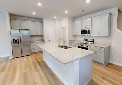 Kitchen with appliances with stainless steel finishes, a sink, gray cabinets, light wood finished floors, and a kitchen island with sink