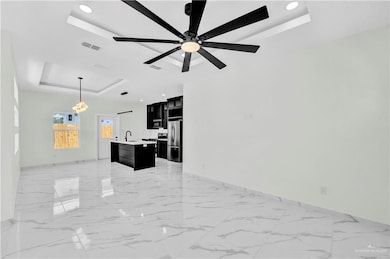 Living room featuring a tray ceiling, ceiling fan with notable chandelier, marble finish floor, and visible vents