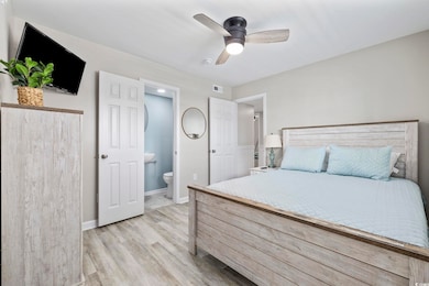 Bedroom with light wood-style floors, a ceiling fan, and ensuite bath